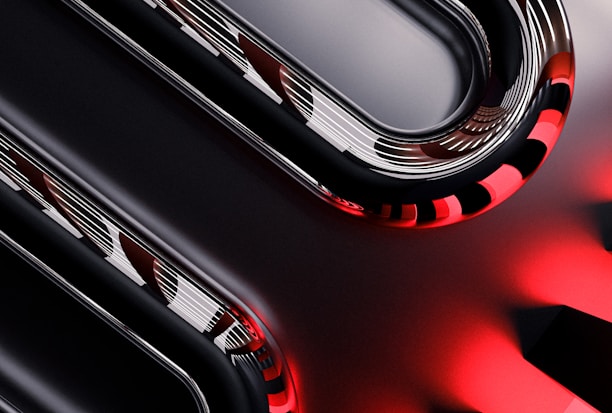 Curved metallic and glossy elements intertwine with smooth, reflective surfaces, displaying a sleek, high-tech appearance. The image incorporates sharp contrasts between dark and light sections, with striking red accents providing a bold visual impact.
