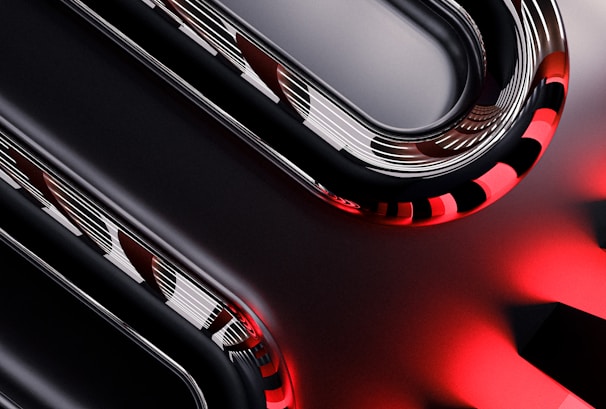 Curved metallic and glossy elements intertwine with smooth, reflective surfaces, displaying a sleek, high-tech appearance. The image incorporates sharp contrasts between dark and light sections, with striking red accents providing a bold visual impact.