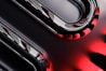 Curved metallic and glossy elements intertwine with smooth, reflective surfaces, displaying a sleek, high-tech appearance. The image incorporates sharp contrasts between dark and light sections, with striking red accents providing a bold visual impact.