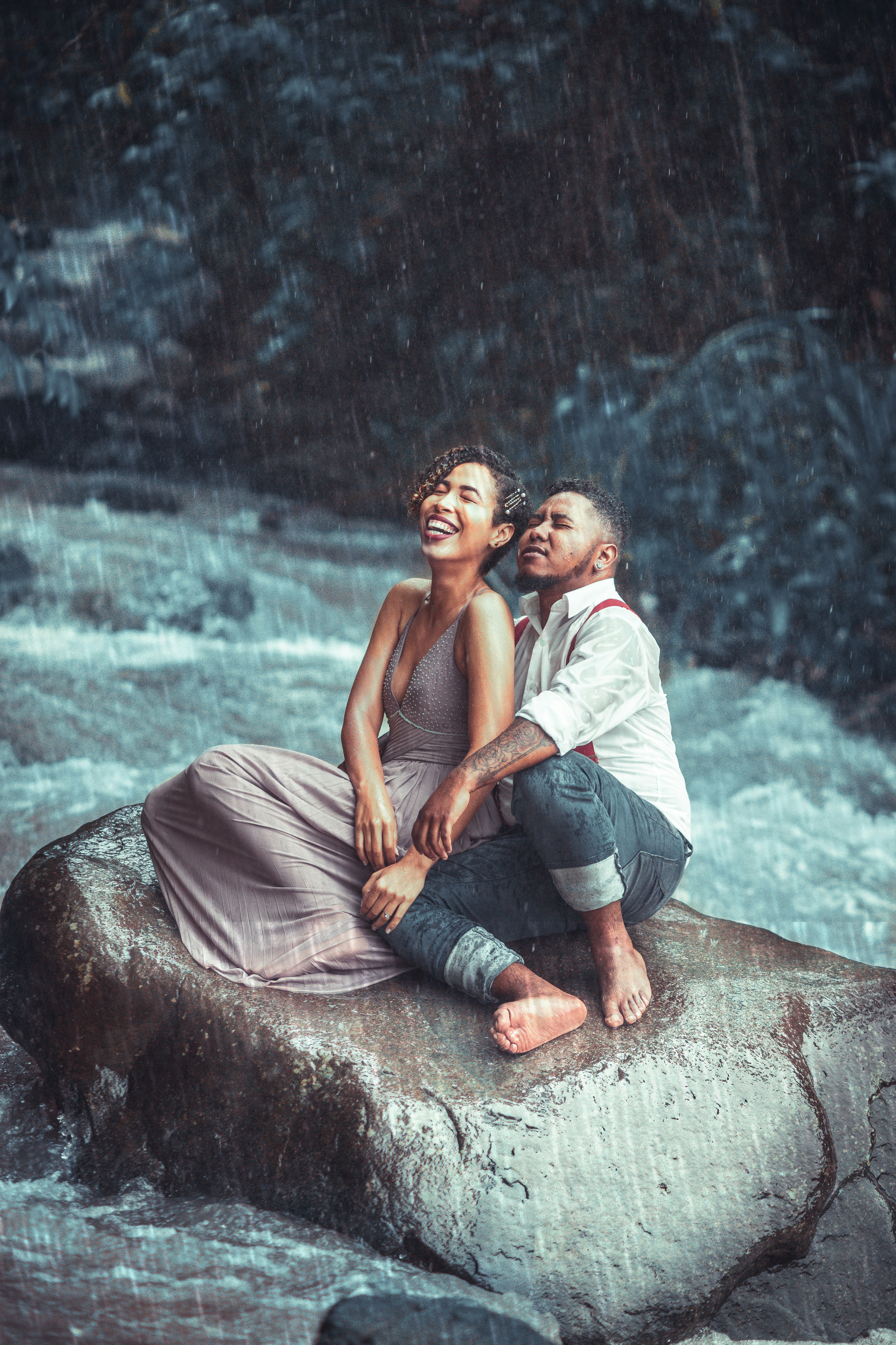 a man and woman sitting on a rock in the rain