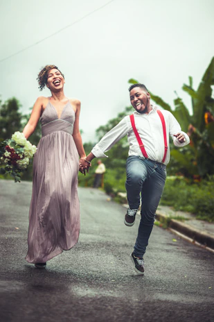 A joyful couple holding hands beneath a colorful umbrella on a rainy street.