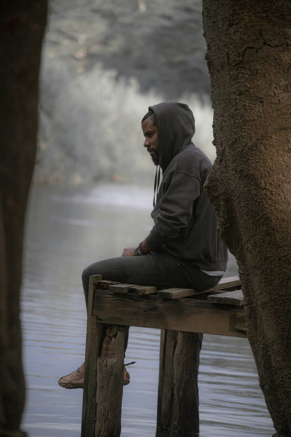 a man sitting on a wooden bench next to a body of water