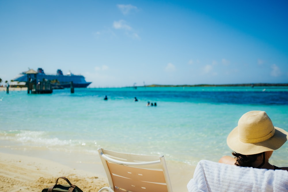 a woman sitting on a beach next to a chair