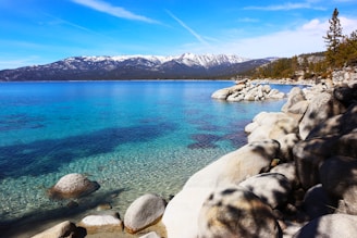 a rocky shore with clear blue water and mountains in the background