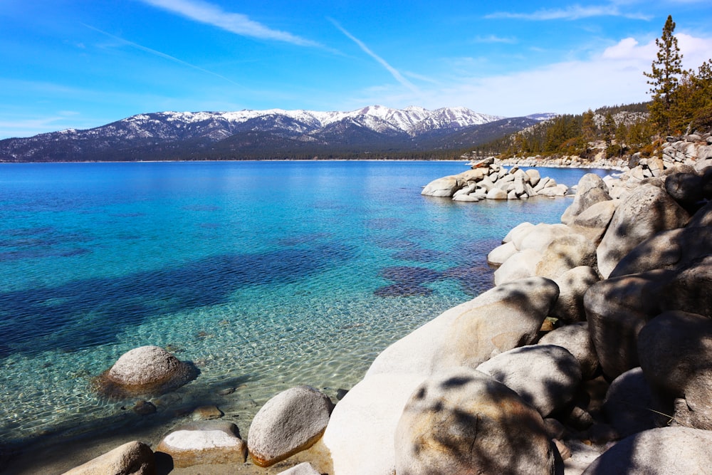 a rocky shore with clear blue water and mountains in the background