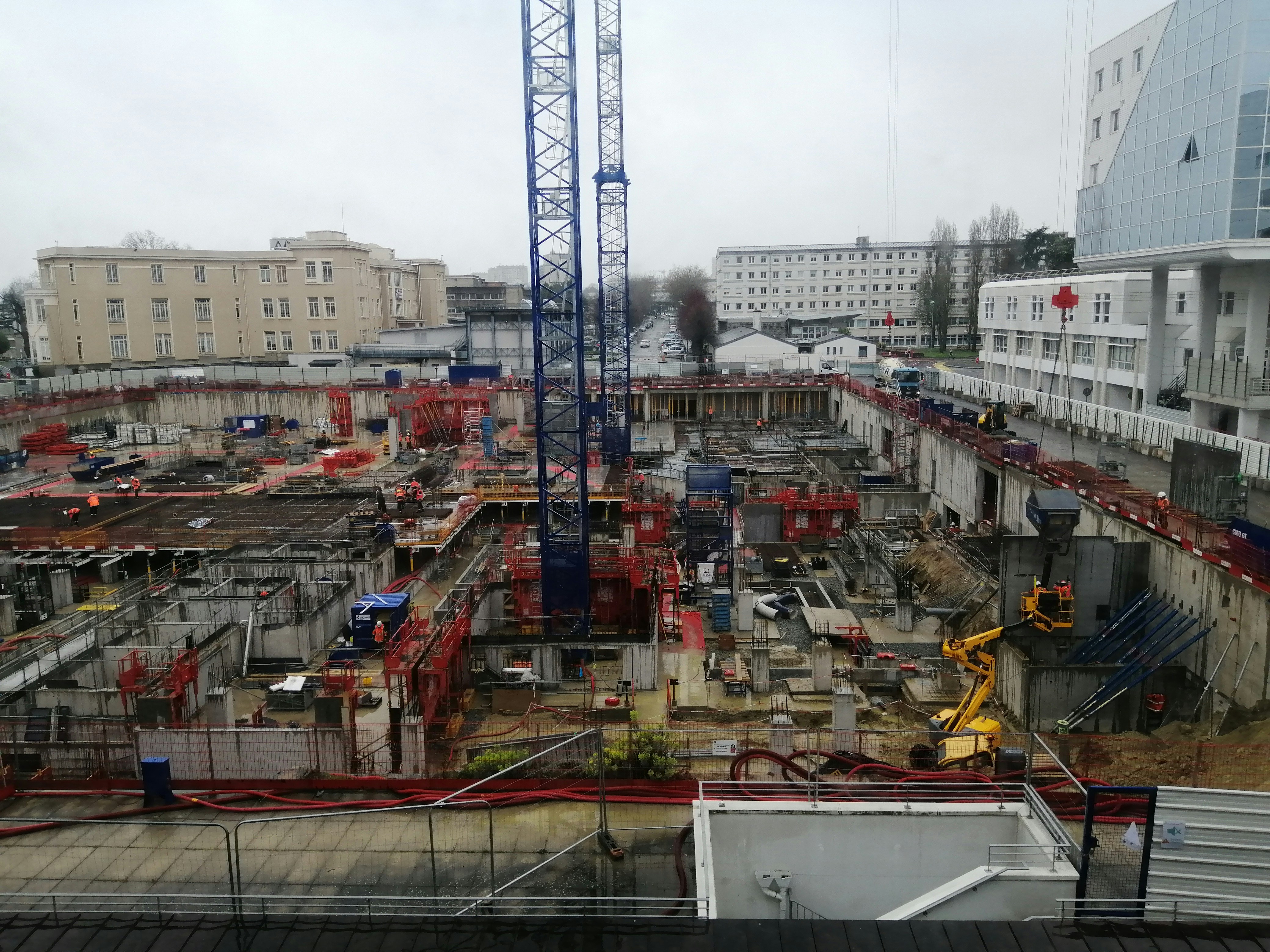 Chantier de construction en cours, grues et structures métalliques, ciel nuageux sombre, atmosphère industrielle
