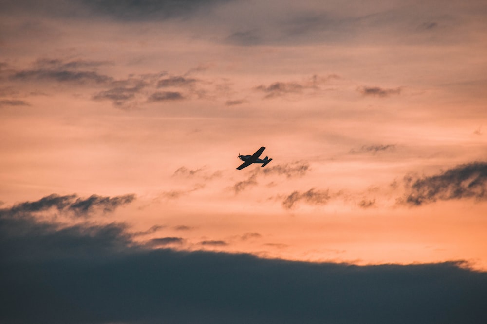 a plane flying through a cloudy sky at sunset