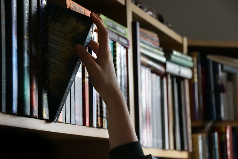 a person reaching for a book on a book shelf