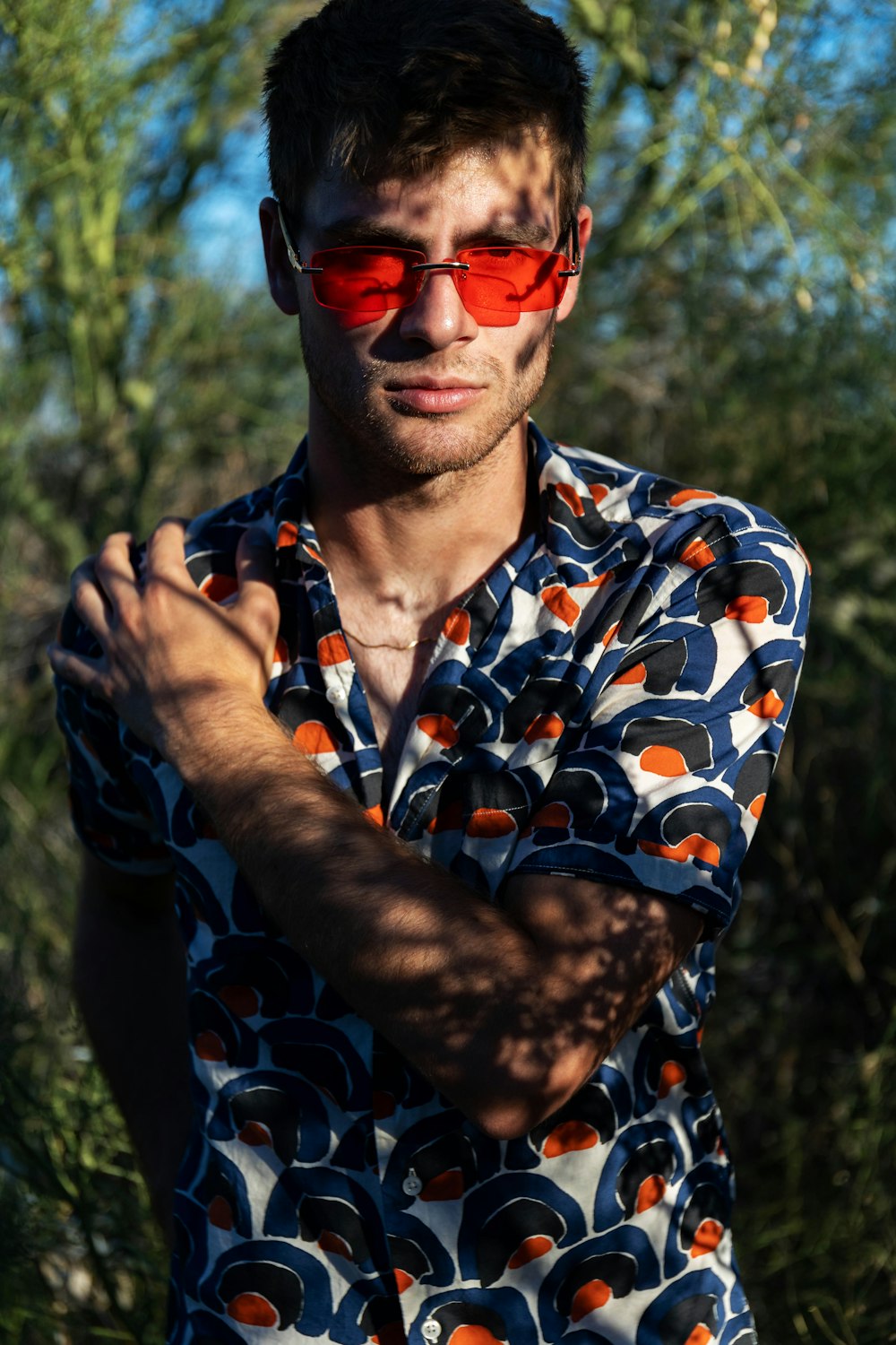 a man wearing red sunglasses standing in front of trees