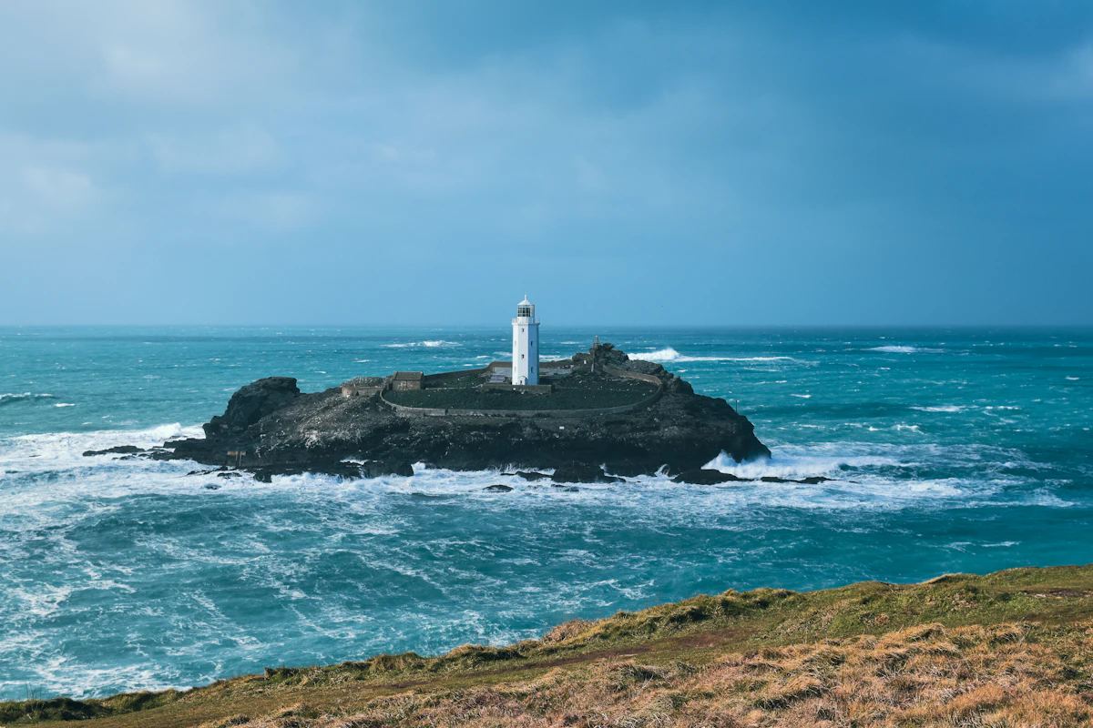 Godrevy Lighthouse on its rock island in a rough grey sea, seen from the grassy headland