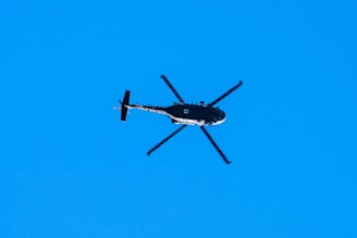 A sleek Robinson R66 helicopter flying against a clear blue sky.