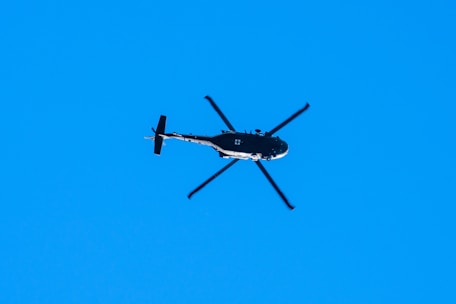 A sleek Robinson R66 helicopter flying against a clear blue sky.
