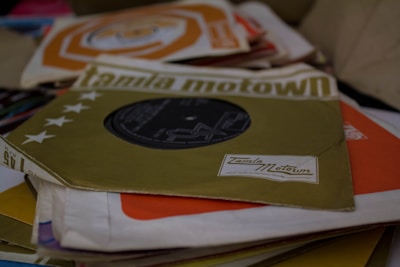 A stack of vintage vinyl records, each in its sleeve, with the top one featuring the Tamla Motown logo. The sleeves display various colors and graphical designs, suggesting a collection of music albums possibly from the Motown era.
