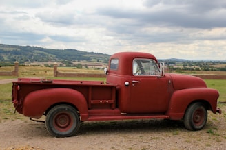 A rustic Idaho farm landscape with mountains in the background and an old red pickup truck parked near a barn.