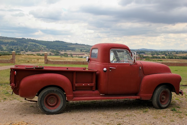 A rustic Idaho farm landscape with mountains in the background and an old red pickup truck parked near a barn.