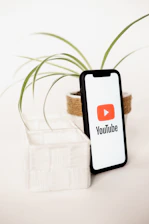 a cell phone sitting next to a plant with a youtube logo on it