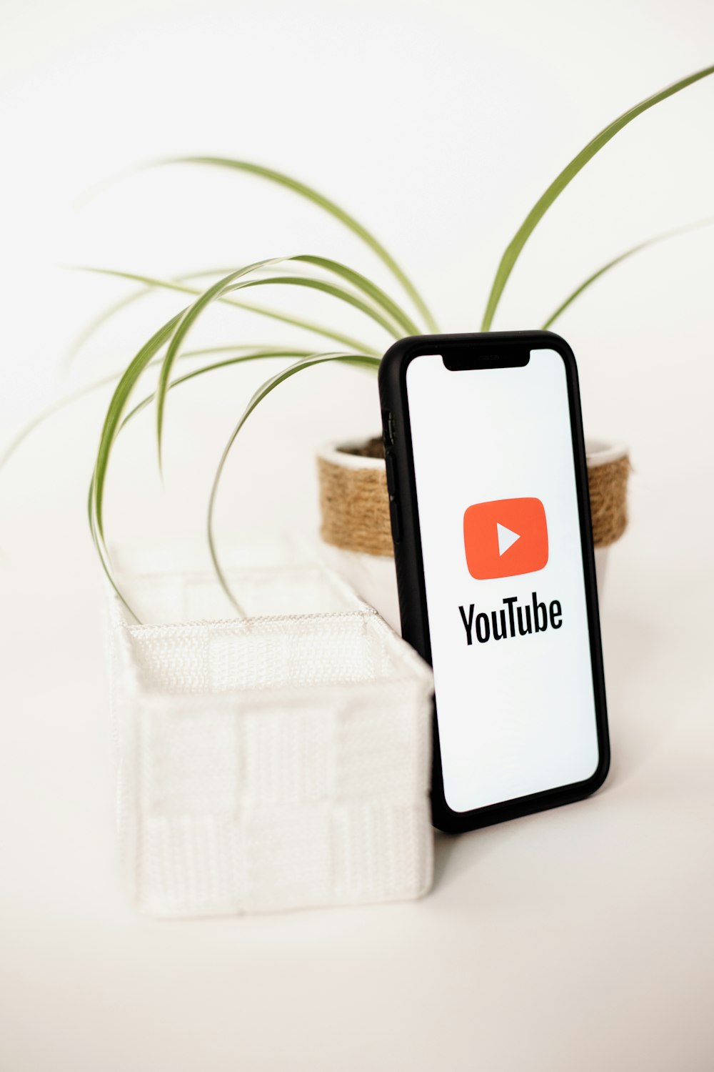 a cell phone sitting next to a plant with a youtube logo on it
