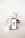 A smartphone displaying the YouTube logo stands upright on a white surface, surrounded by two small potted plants. The plant on the right has long, slender green leaves and is in a white pot wrapped with a brown band, creating a visually pleasing composition.