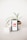 A smartphone displaying the YouTube logo stands upright on a white surface, surrounded by two small potted plants. The plant on the right has long, slender green leaves and is in a white pot wrapped with a brown band, creating a visually pleasing composition.