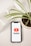A smartphone displaying the YouTube logo is placed on a light-colored surface. To the side, there is a potted plant with green, slender leaves. The pot is filled with dark soil and positioned next to a rectangular white container.