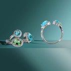A stylish display of rings featuring green gemstones on a leafy green backdrop.