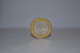 A single coin stands upright on a smooth, light-colored surface against a plain background. The coin has a silver center with an intricate emblem, surrounded by a gold outer ring. The year 1995 and some text are embossed on it.