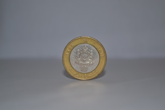 A single coin stands upright on a smooth, light-colored surface against a plain background. The coin has a silver center with an intricate emblem, surrounded by a gold outer ring. The year 1995 and some text are embossed on it.