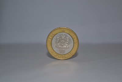 A single coin stands upright on a smooth, light-colored surface against a plain background. The coin has a silver center with an intricate emblem, surrounded by a gold outer ring. The year 1995 and some text are embossed on it.