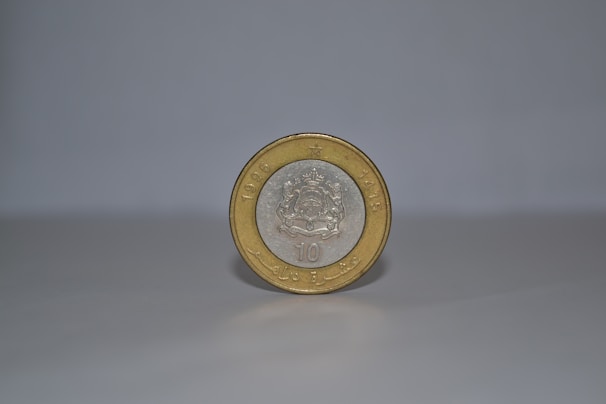 A single coin stands upright on a smooth, light-colored surface against a plain background. The coin has a silver center with an intricate emblem, surrounded by a gold outer ring. The year 1995 and some text are embossed on it.