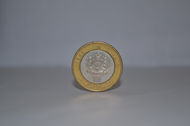 A single coin stands upright on a smooth, light-colored surface against a plain background. The coin has a silver center with an intricate emblem, surrounded by a gold outer ring. The year 1995 and some text are embossed on it.