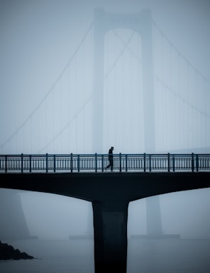 balance and symmetry for photo composition,how to photograph a man walking on a bridge in the foreground, with another big bridge in the background that is shrouded in fog.; a person walking across a bridge in the fog