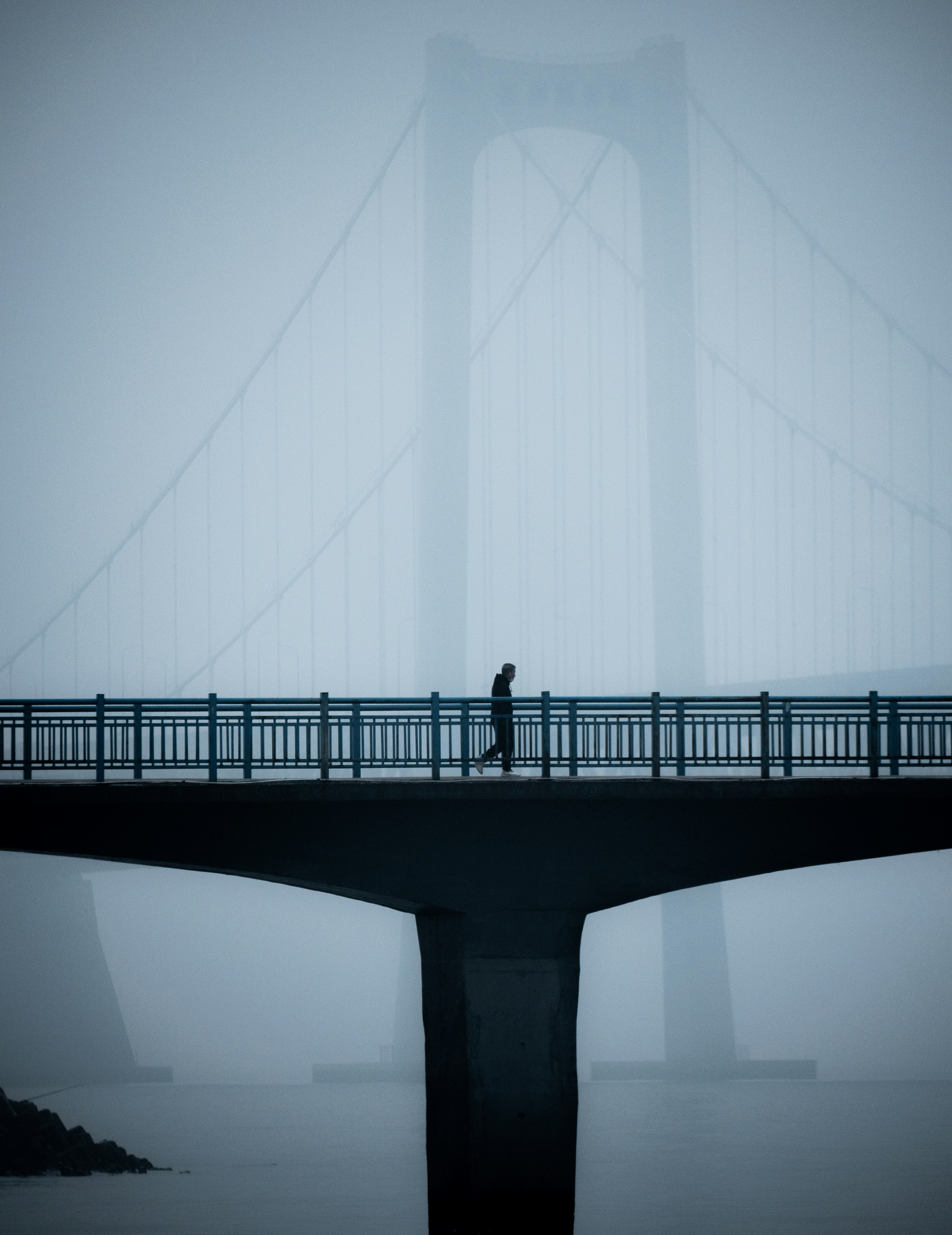 great photo recipe,how to photograph a man walking on a bridge in the foreground, with another big bridge in the background that is shrouded in fog.; a person walking across a bridge in the fog