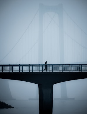 balance and symmetry for photo composition,how to photograph a man walking on a bridge in the foreground, with another big bridge in the background that is shrouded in fog.; a person walking across a bridge in the fog