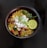 A bowl of poha garnished with grated coconut, peanuts, curry leaves, a lemon wedge, and cilantro is placed against a dark background.