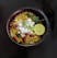 A bowl of poha garnished with grated coconut, peanuts, curry leaves, a lemon wedge, and cilantro is placed against a dark background.