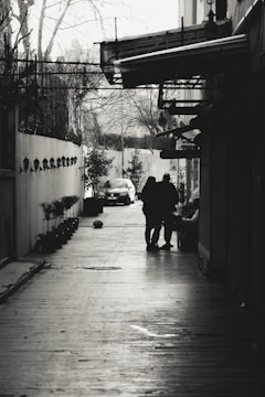 A cinematic film scene showing a tense moment between two characters in a rain-soaked alley.