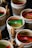 A collection of small cups hold assorted tea bags, including a prominent green and yellow Twinings packet. Some cups are tied with twine and sticks of cinnamon are placed alongside the packets, enhancing the rustic presentation.