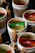 A collection of small cups hold assorted tea bags, including a prominent green and yellow Twinings packet. Some cups are tied with twine and sticks of cinnamon are placed alongside the packets, enhancing the rustic presentation.