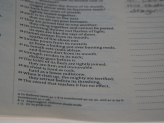A close-up of a page in a book with text printed in a vertical column. The text appears to be excerpted lines of a poem or scripture, with numbers at the beginning of each line. The text is bordered by a dotted line on the right, with a lined blank space next to it for notes. Some handwritten text is visible at the top right corner.