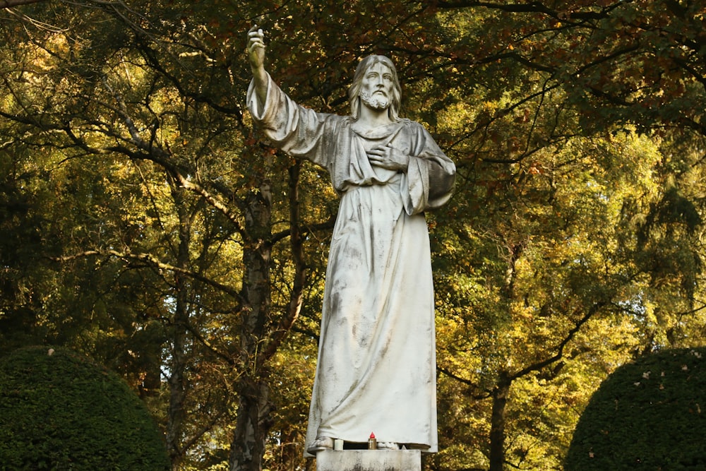 a statue of jesus in a park surrounded by trees
