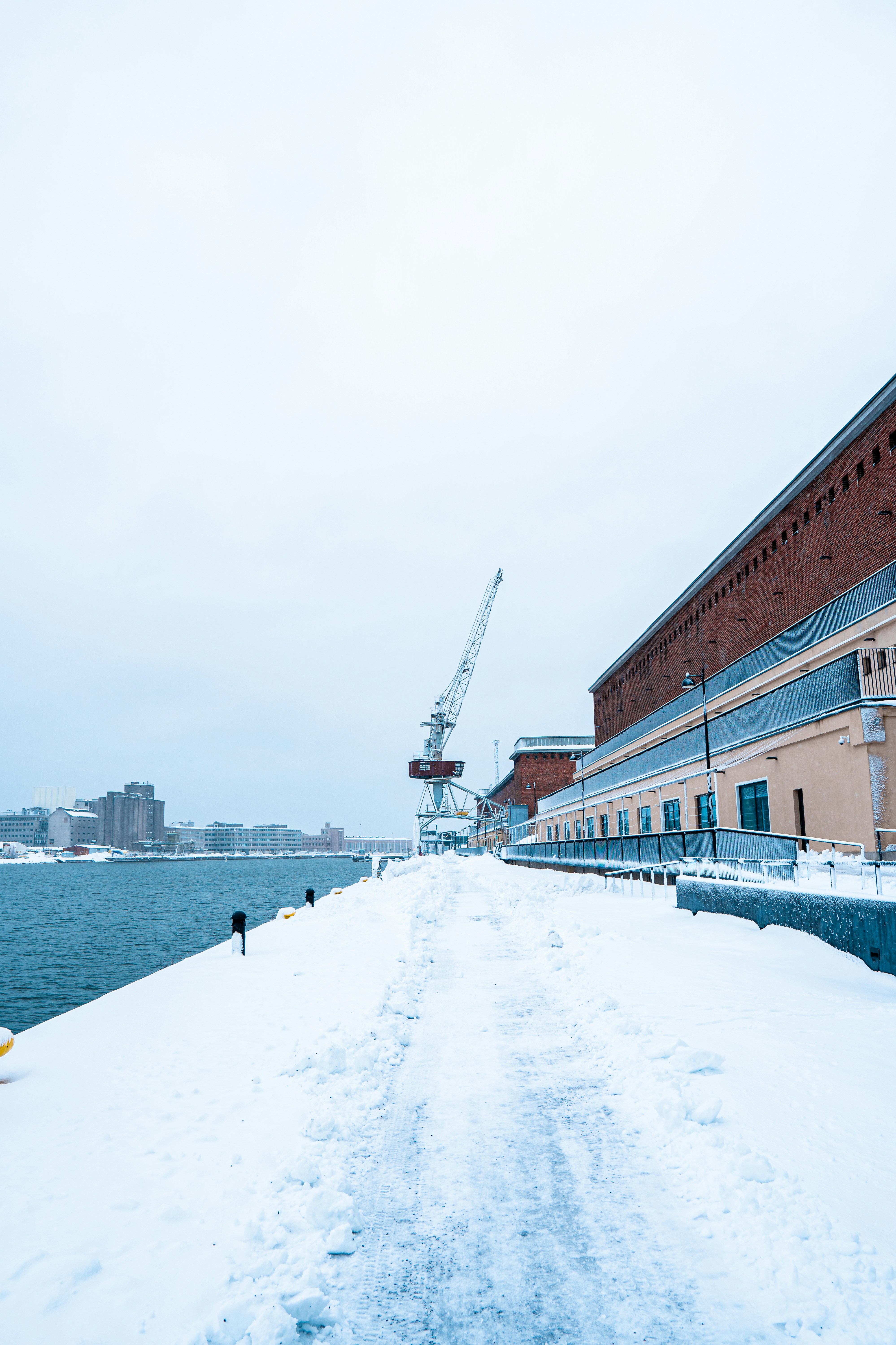 a man walking down a snow covered sidewalk next to a body of water