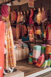 a woman sitting in front of a store filled with colorful items
