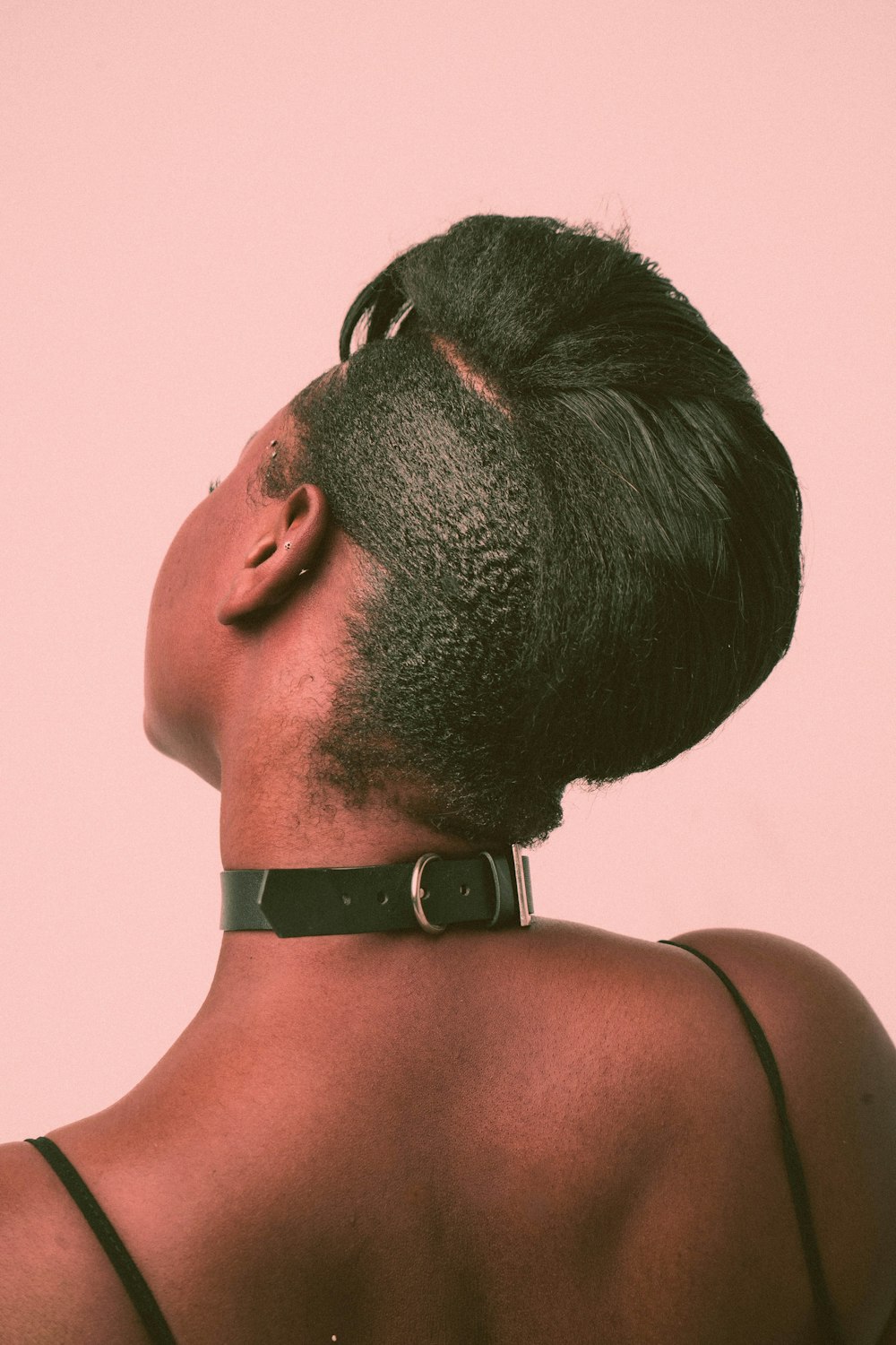 a woman with a shaved head wearing a leather choker