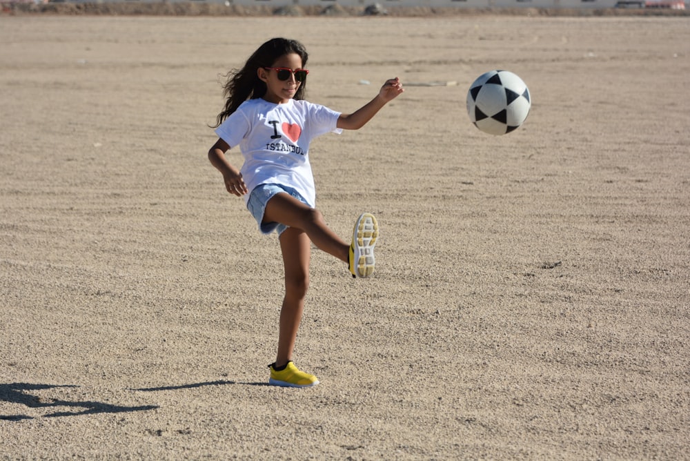 a young girl kicking a soccer ball on the beach
