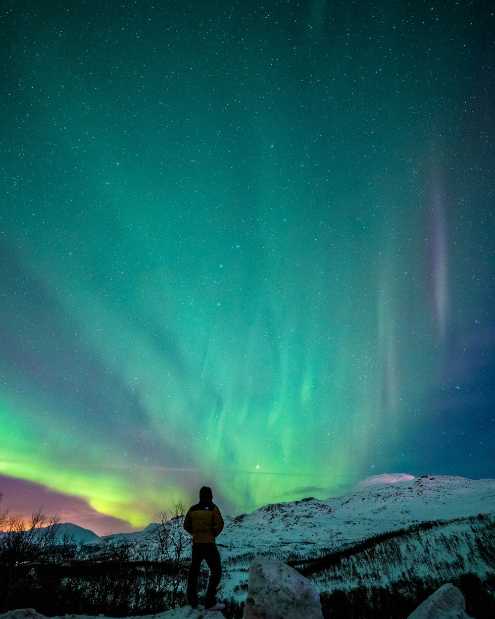 a man standing on top of a snow covered slope under a green and purple sky