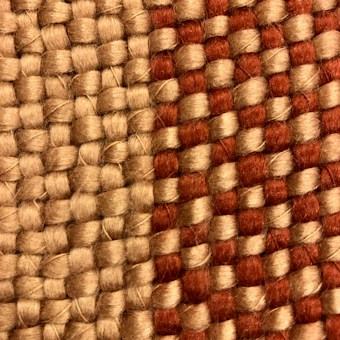 A close-up view of a woven fabric featuring interlocking strands of beige and reddish-brown threads. The texture of the fabric is coarse, highlighting the thick yarns used in the weaving process.