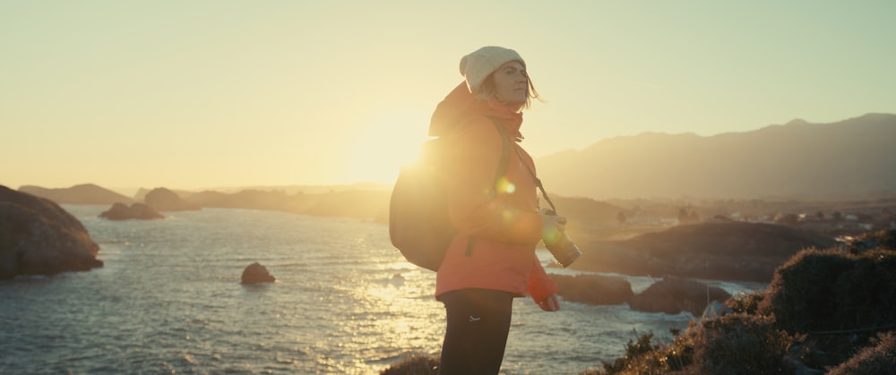 a woman standing on top of a hill next to the ocean