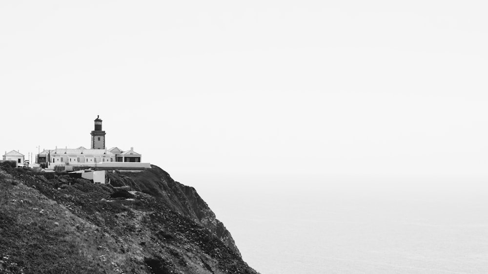 a black and white photo of a lighthouse on a cliff