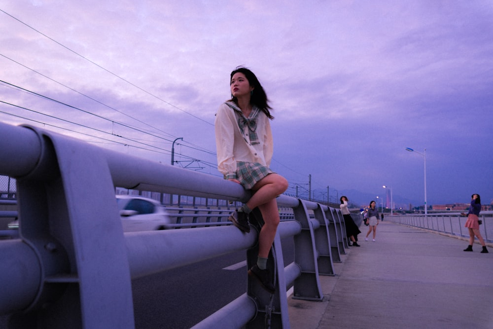 a woman is sitting on a rail by the road