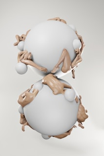 A surreal composition with two large, smooth, white spheres positioned vertically. Human figures are intertwined around and between the spheres, creating a dynamic and complex arrangement. The figures appear to have smooth, featureless heads, emphasizing an abstract, artistic style.
